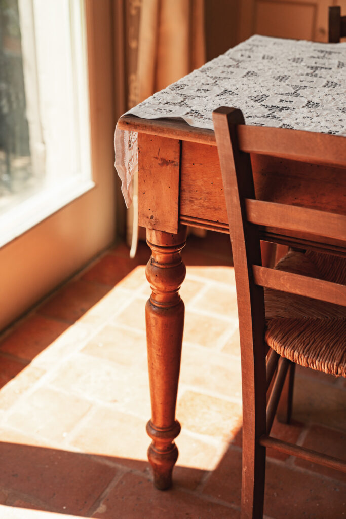Particolare della gamba di un tavolo in legno antico e della sedia abbinata, dal top del tavolo scende un pizzo ricamato a mano.