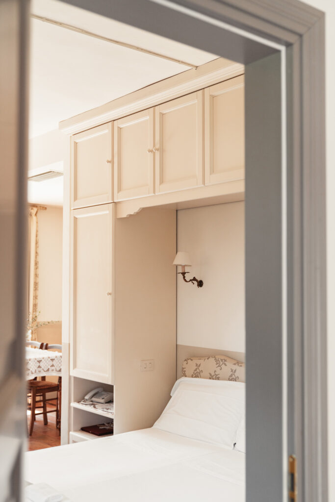 Da una porta aperta si vede parte di un letto matrimoniale sotto un armadio a ponte e parte di un tavolo legno con sedie.