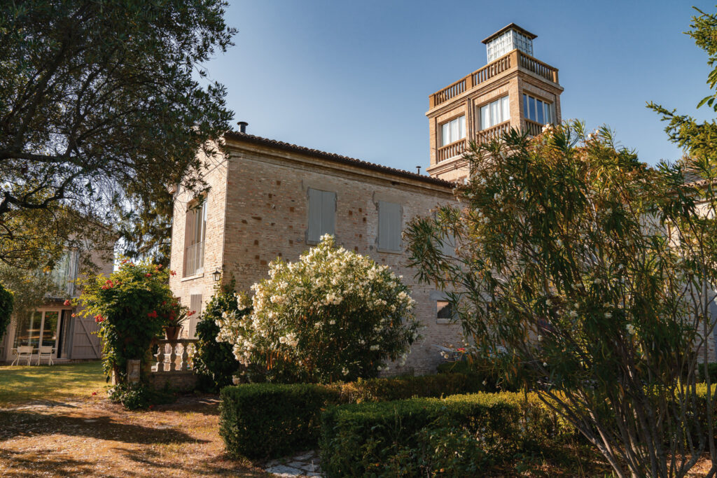 Il Pignocco farmhouse surrounded by lush vegetation and flowering trees.