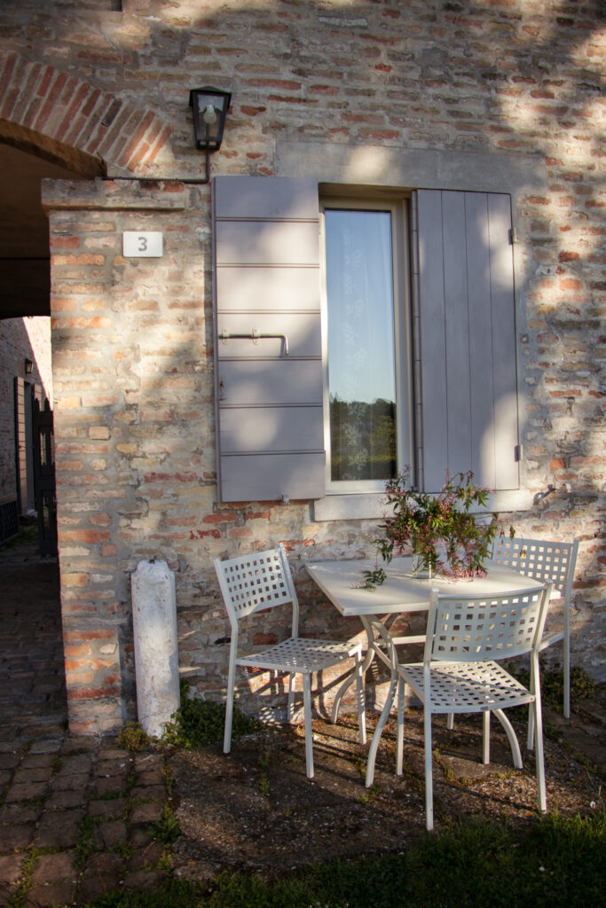 White metal garden table with a flower vase and three chairs, placed in front of the farmhouse under the studio window.