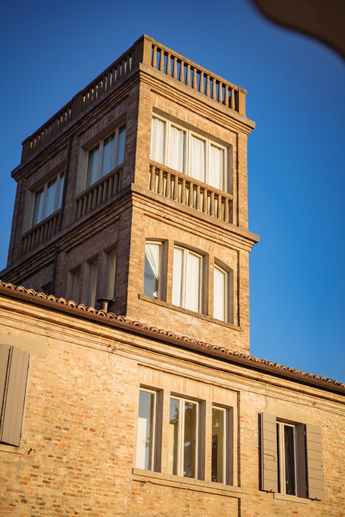 Una torre belvedere, con finestre a tutta altezza e composta da due piani e tetto terrazzato, si eleva sopra un casale antico.