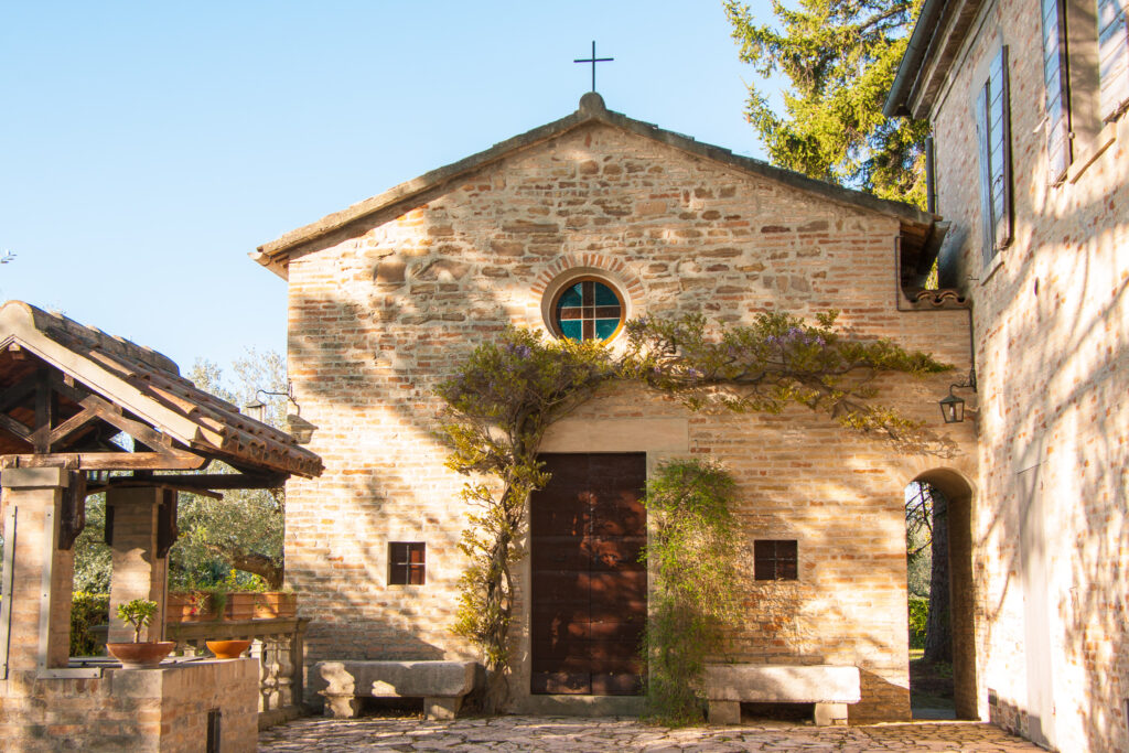 Private chapel on the hill of San Pietro in Calibano, with two stone benches and small windows flanking the main door, and a rose window above.