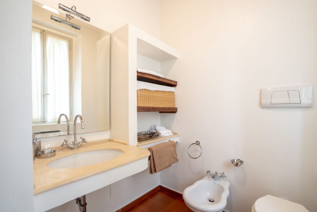 Bagno con lavabo all'interno di una piana in marmo, specchio con lampada, mensole di legno e cesto in vimini