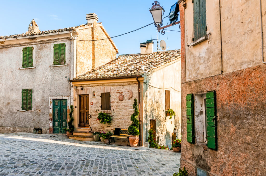 Una piccola casa antica a Montefabbri, un grazioso borgo nelle Marche italiane, con vasi di piante all’esterno e una panchina in legno che invita al riposo e al relax.