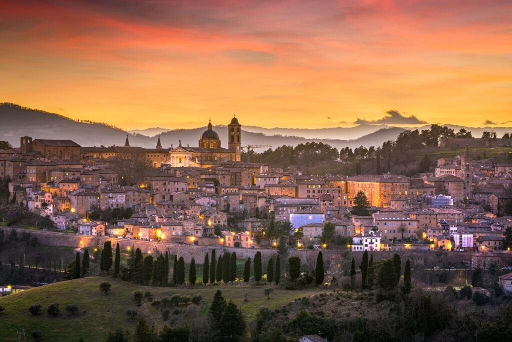 La città rinascimentale di Urbino, nelle Marche, dall'alto, con i tetti delle case antiche, la cupola della cattedrale, le torri e gli alberi e le montagne tutto intorno.