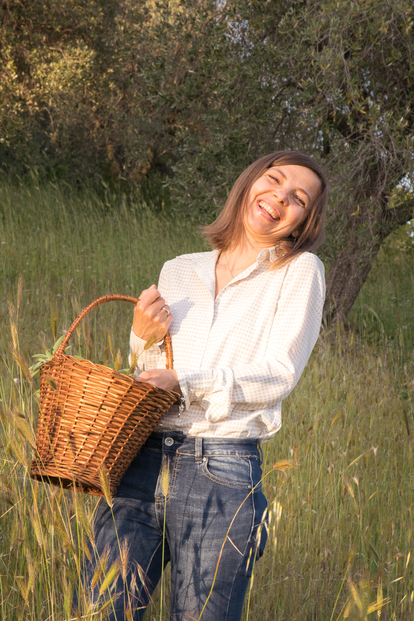 Una donna in campagna ride mentre trasporta un cestino per raccogliere erbe aromatiche