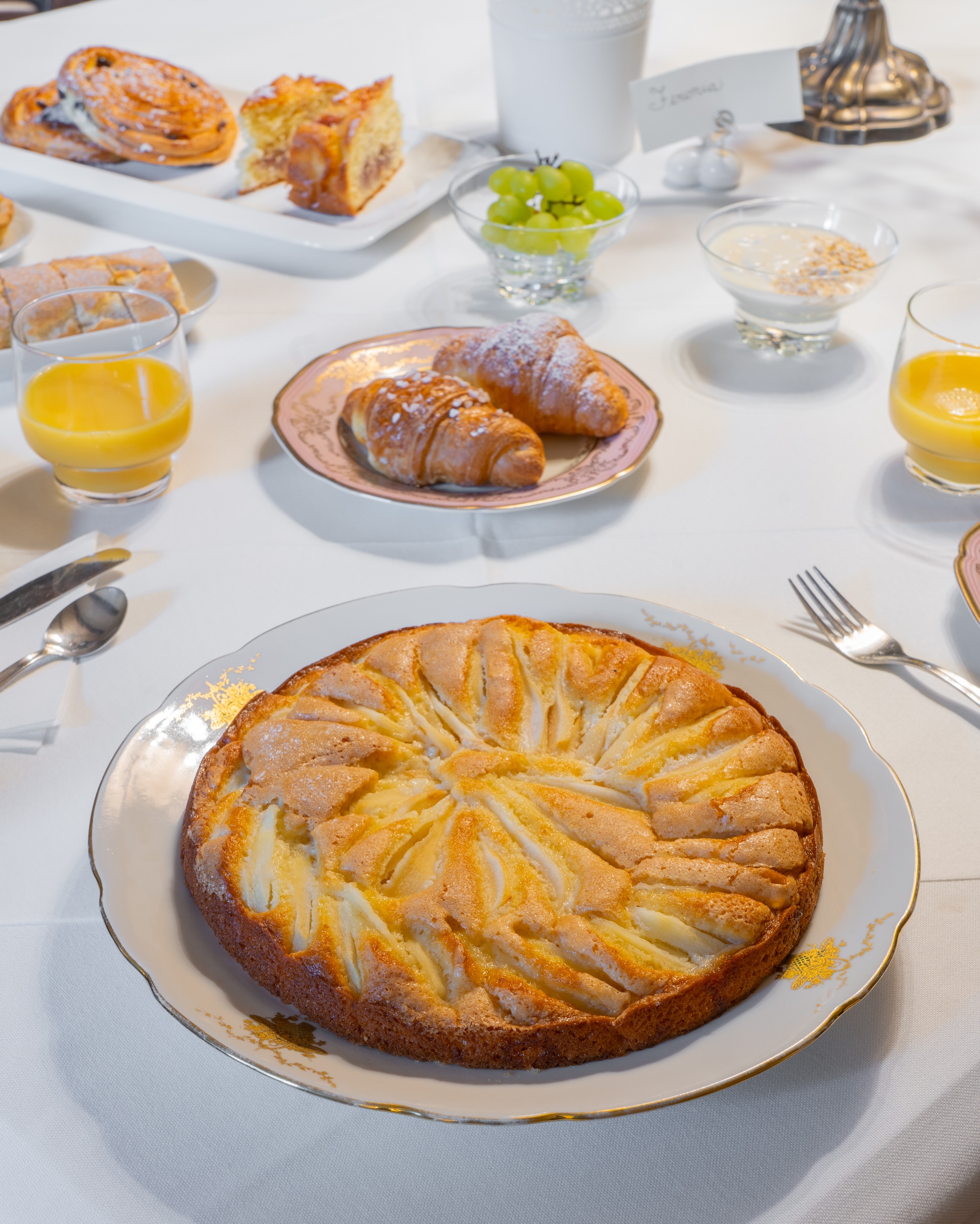 Torta di pere al centro del tavolo, sullo sfondo bicchere succo di arancia, briosce
