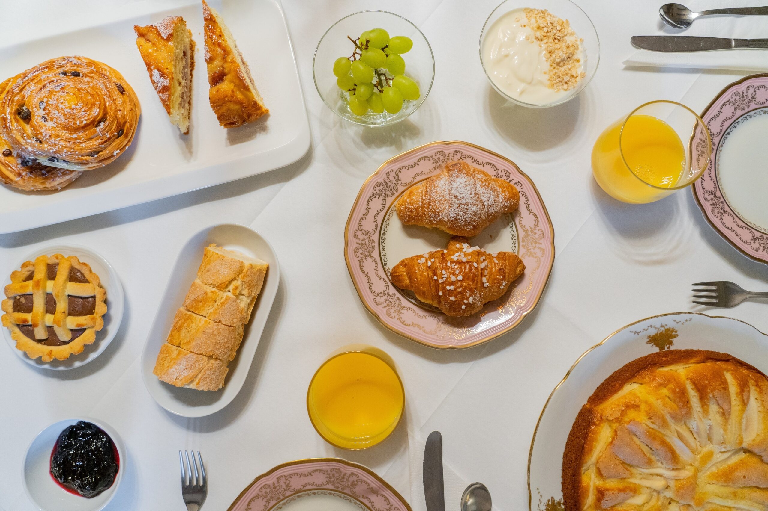 Buffet colazioni con briosce, yogurt con muesli, crostata alla cioccolata, pane fresco, marmellata, succo d'arancia, torta di pere, uva