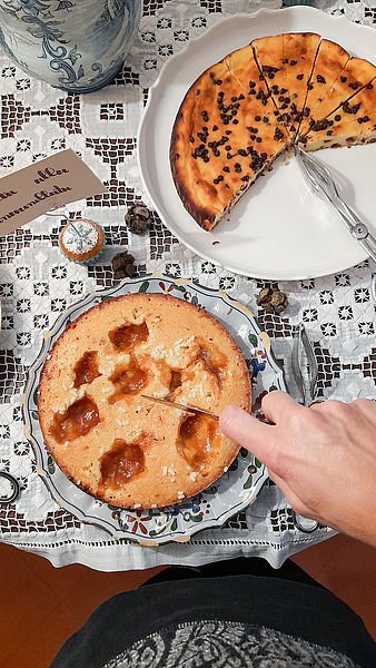 La mano dell'host del B&B taglia una fetta d torta morbida con zucchero in granella e marmellata.